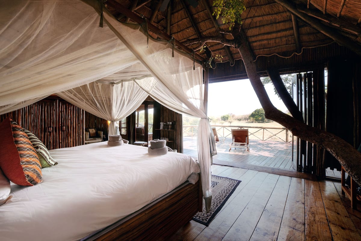 A bed with a canopy, wooden flooring, and a view of the outdoors.