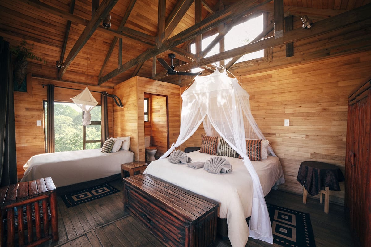 A wooden cabin with two beds, a ceiling fan, and a large window.