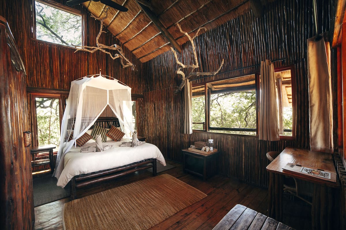 A rustic wooden room with a bed, a small table, and a window with curtains.