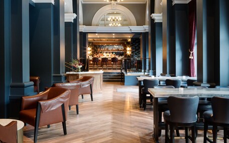 A spacious lobby with high ceilings, elegant chandeliers, and a bar area in the background.