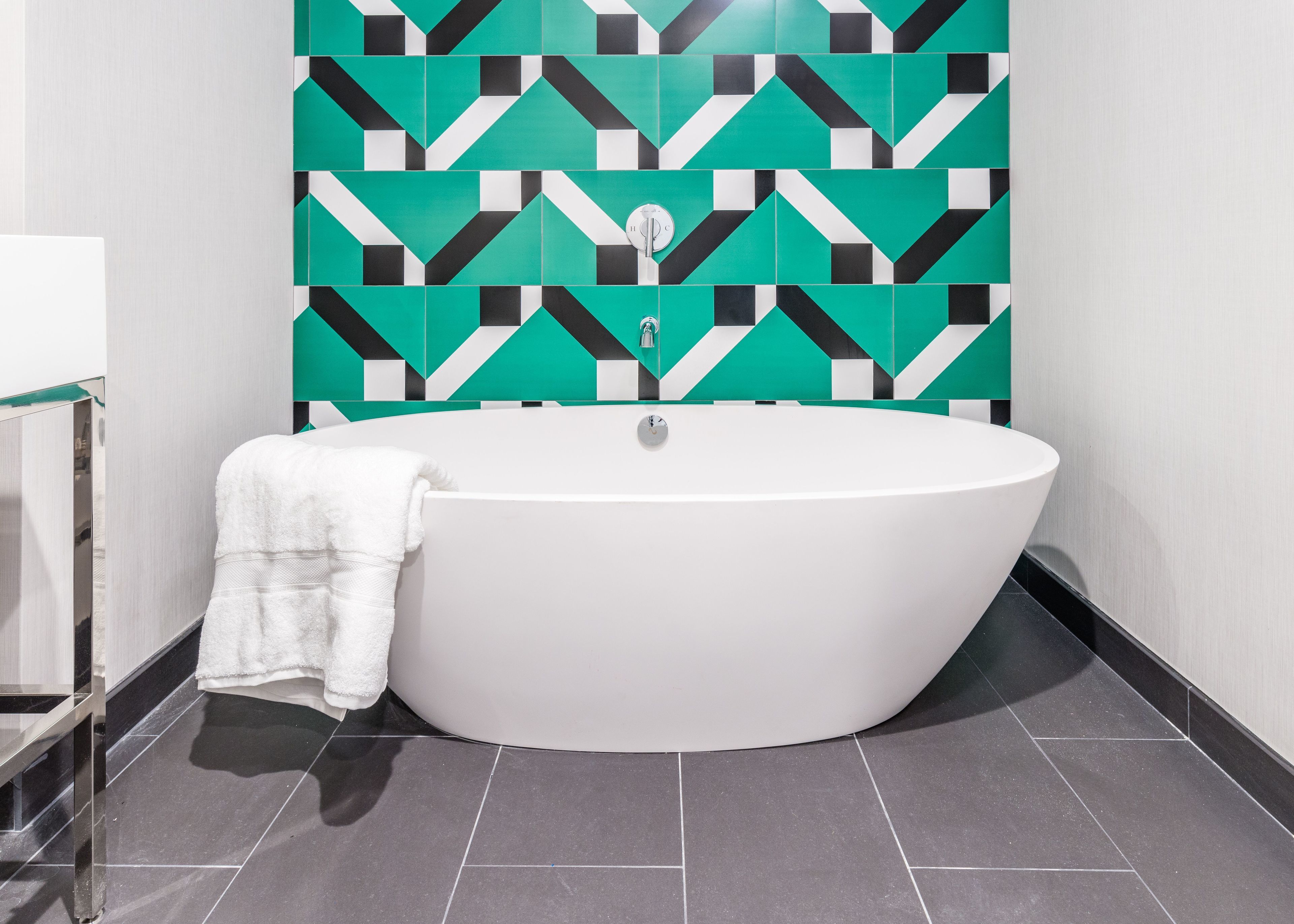Ein modernes Badezimmer mit einer freistehenden Badewanne, einem Handtuch und einer Wand mit geometrischem Muster.