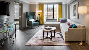A hotel room with a bed, a sofa, a desk with a chair, a standing lamp, and a TV. - The Darcy Hotel (Washington)