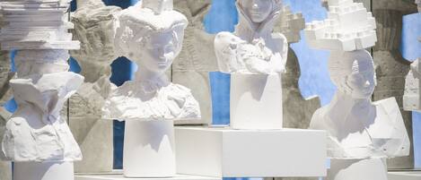 A display of white sculptures on pedestals in a modern interior with blue walls and a chandelier.