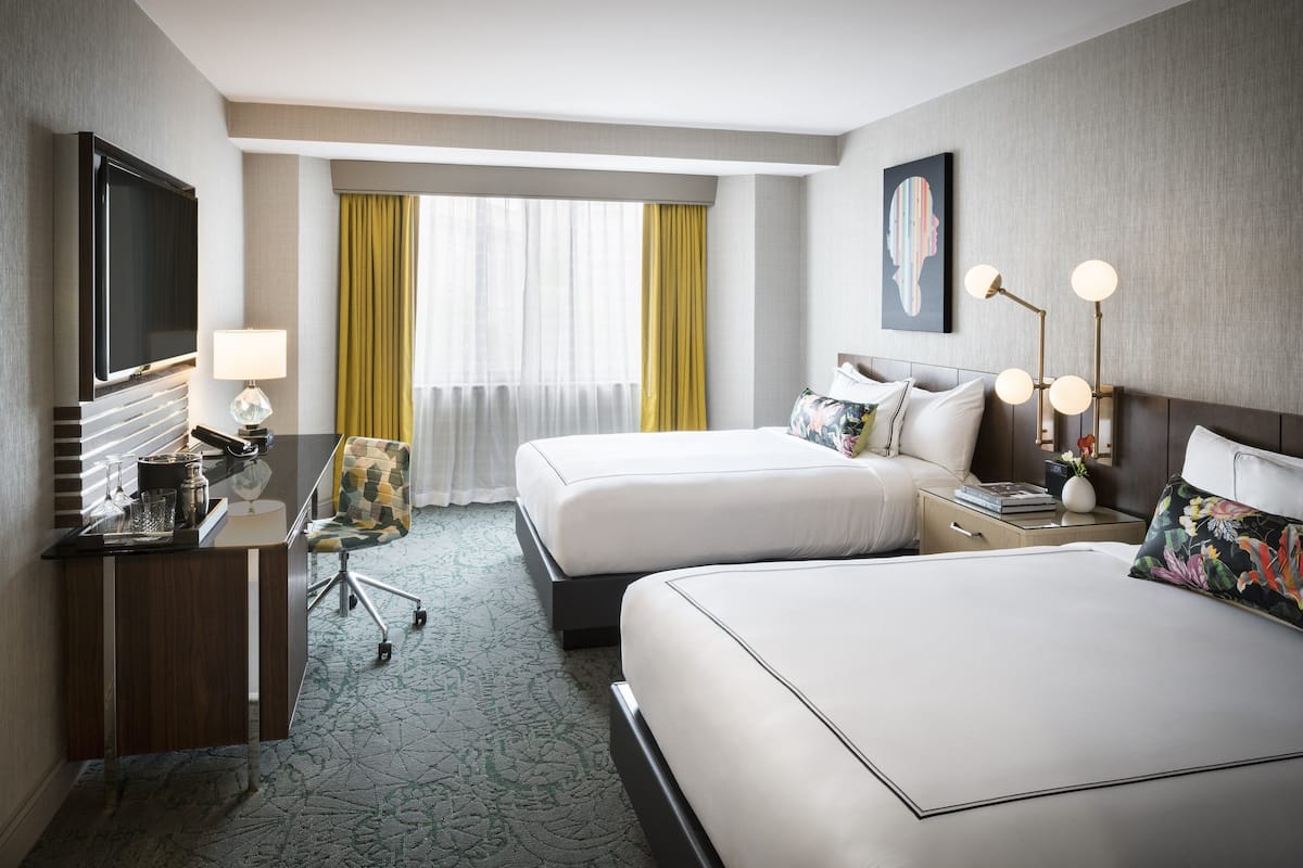 A hotel room with two beds, a desk, a TV, and a window with curtains.