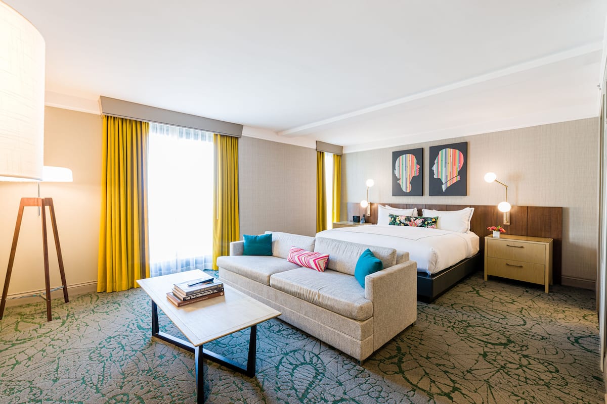 A hotel room with a bed, a sofa, a desk, and a nightstand.