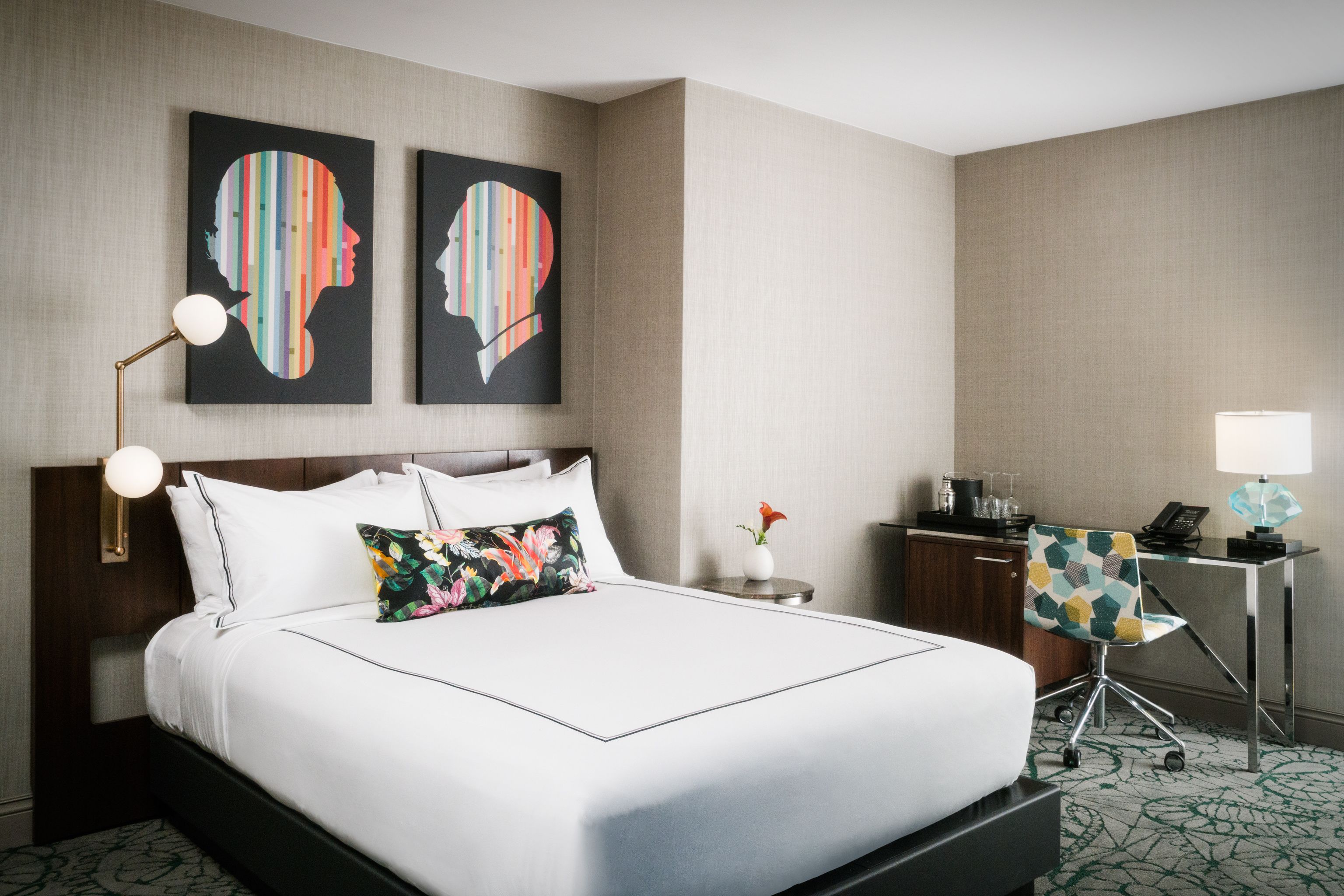 A hotel room with a large bed, a desk, a chair, and two wall art pieces.