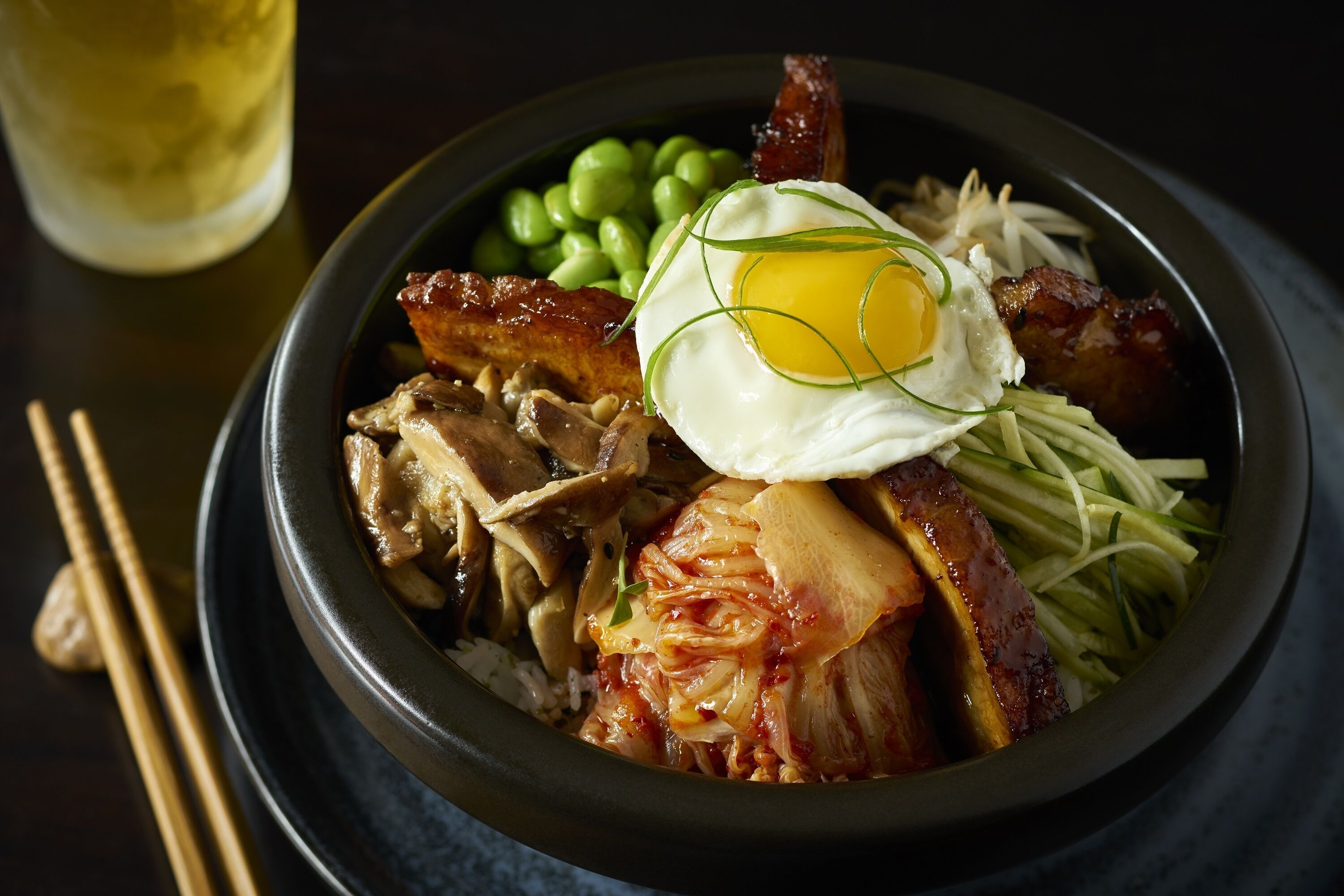 A bowl of food with various ingredients including meat, vegetables, and a fried egg.