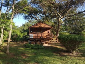 A rustic wooden cabin with a porch, surrounded by lush greenery and trees. - Thokozani Lodge (Mbombela)