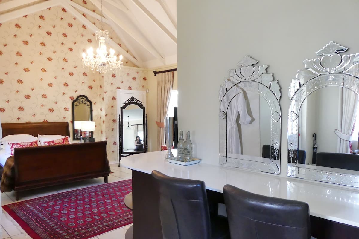 A bedroom with a bed, a large mirror, a chandelier, and a red patterned rug.
