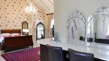 A bedroom with a bed, a large mirror, a chandelier, and a red patterned rug.