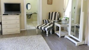 Une pièce avec une télévision posée sur une commode, un fauteuil à rayures, une petite table avec un miroir et une porte donnant sur une salle de bain.