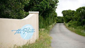 Une route menant à une propriété appelée « The Plantation », avec une pancarte fixée sur un mur de couleur beige.