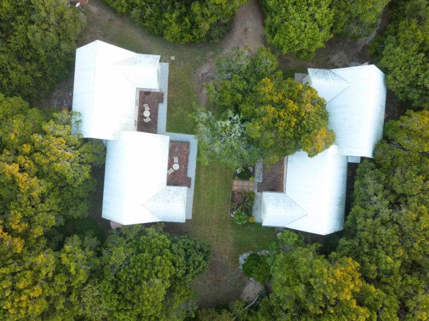Vista aérea de uma propriedade com quatro estruturas de telhado branco, cercada por vegetação densa.
