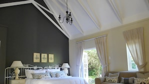Une chambre à coucher comprenant un lit, des tables de chevet, un canapé, un lustre et une fenêtre avec des rideaux.