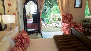 A hotel room with a bed, a chair, a table, and a view of the garden.
