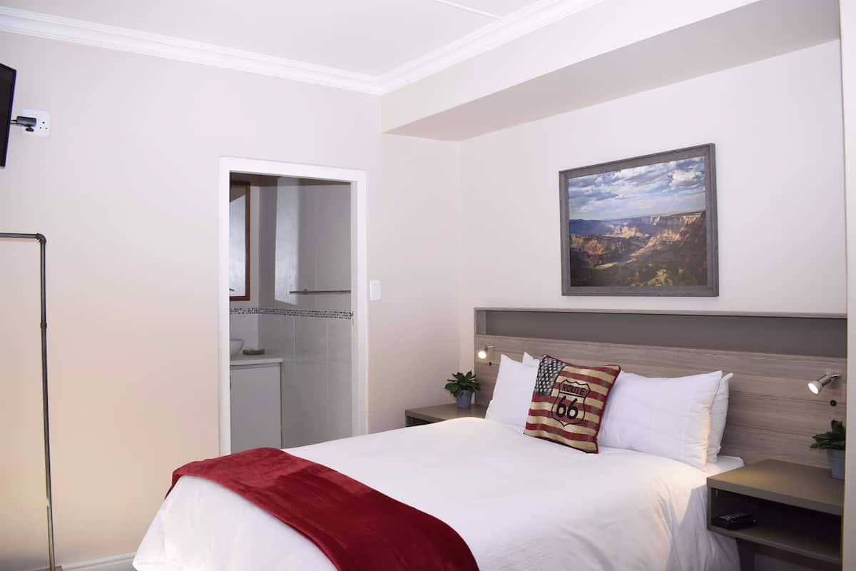 A hotel room with a bed, a nightstand, a wall-mounted TV, and a door leading to a bathroom.