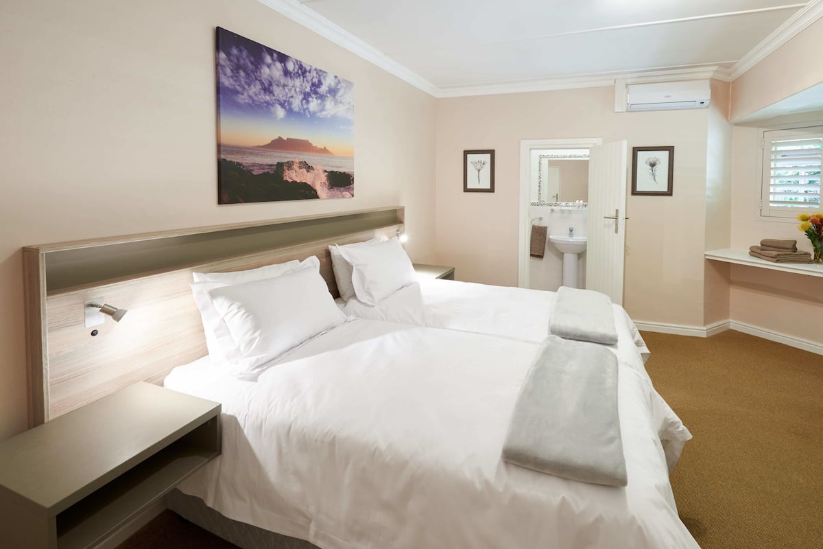 A hotel room with a large bed, bedside tables, a nightstand, a wall-mounted air conditioner, a sink, and a framed picture.
