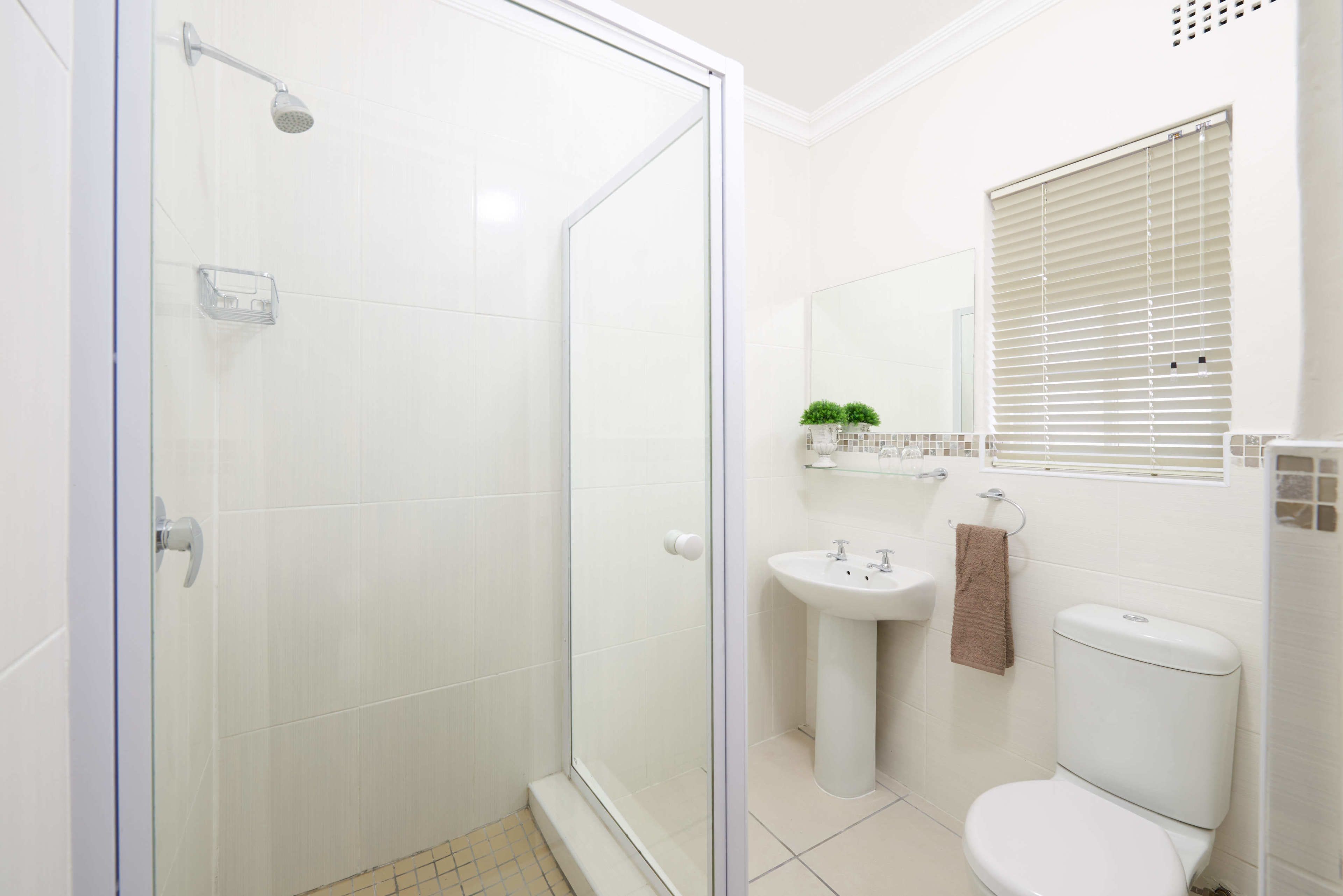 A modern bathroom with a glass-enclosed shower, a pedestal sink, and a toilet.