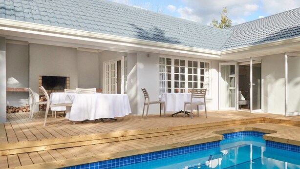 A pool area with a wooden deck, white tables and chairs, and a clear blue pool. - Outeniqua Inn (George)
