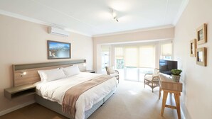 A bedroom with a bed, bedside table, TV, and a view of the outdoors. - Outeniqua Inn (George)