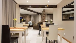 A modern dining area with a brick accent wall, a fireplace, and a television in the background. - Tsitsikamma Manor (Storms River)