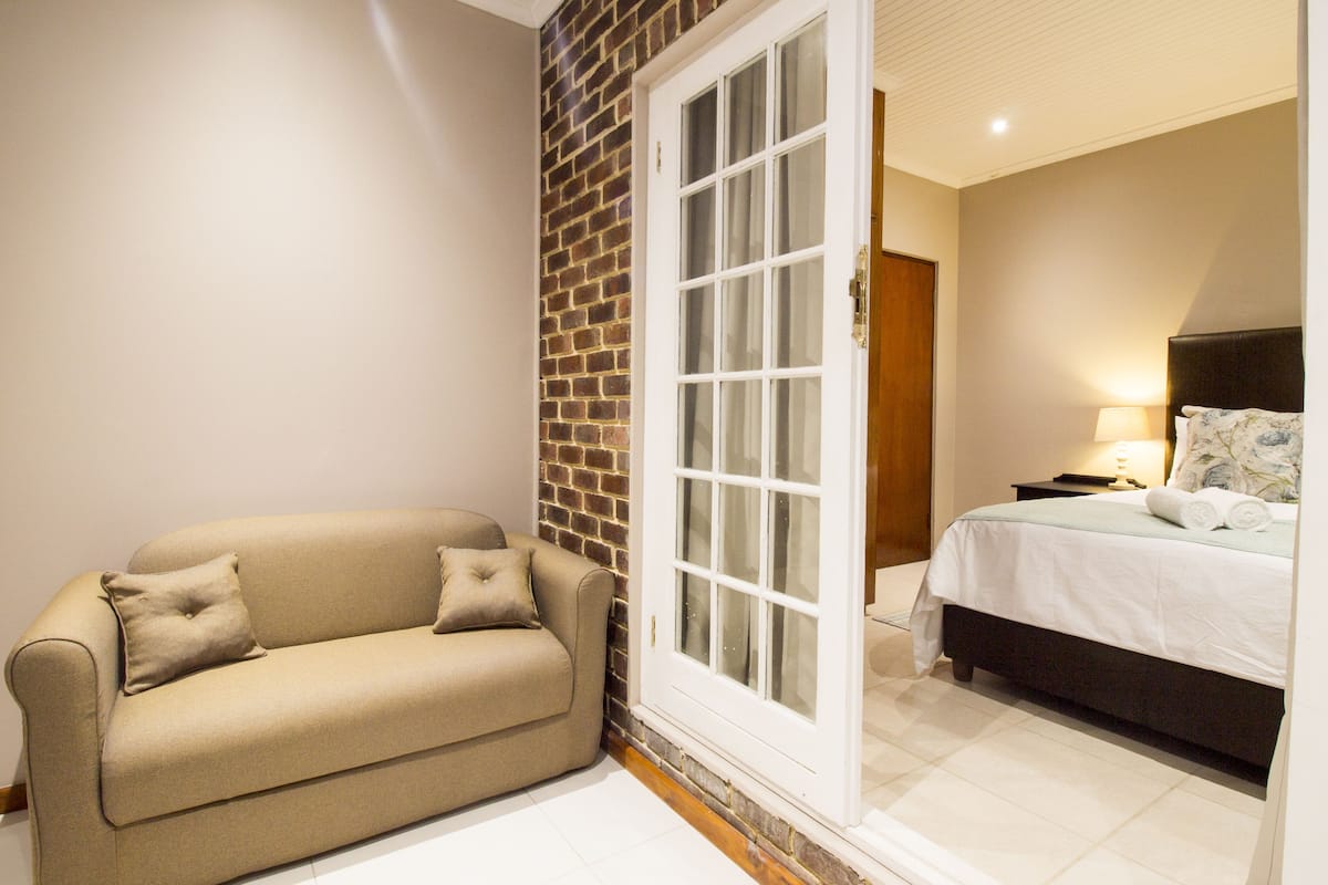 A room with a beige sofa, a bed with a white bedspread, and a brick wall.
