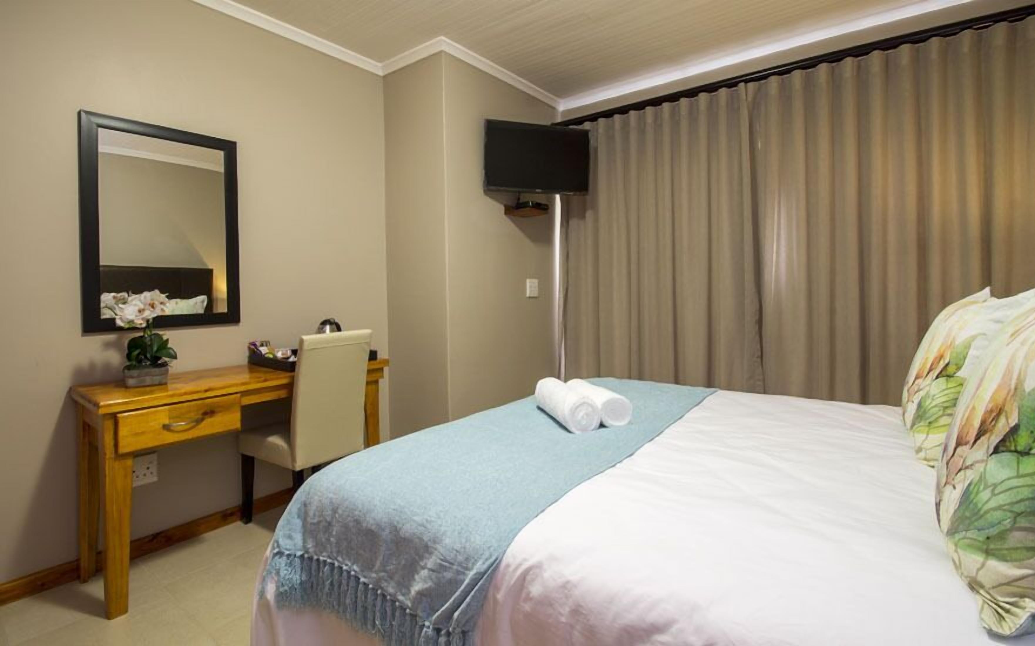 Habitación de hotel con cama, escritorio, silla, televisor de pantalla plana y un ventanal con cortinas.