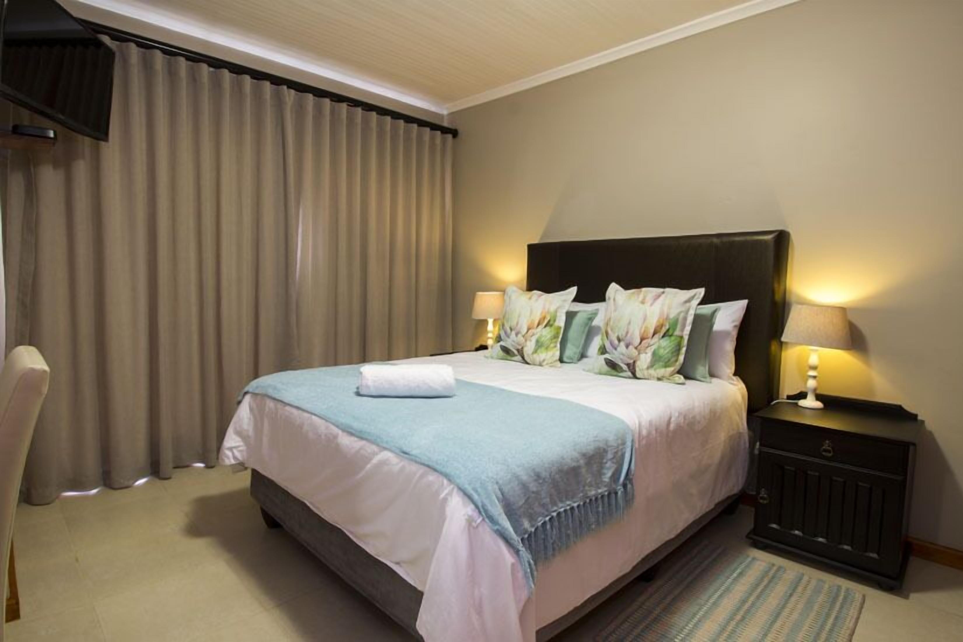 Une chambre d’hôtel avec un grand lit, une table de chevet, une chaise et un téléviseur fixé au mur.