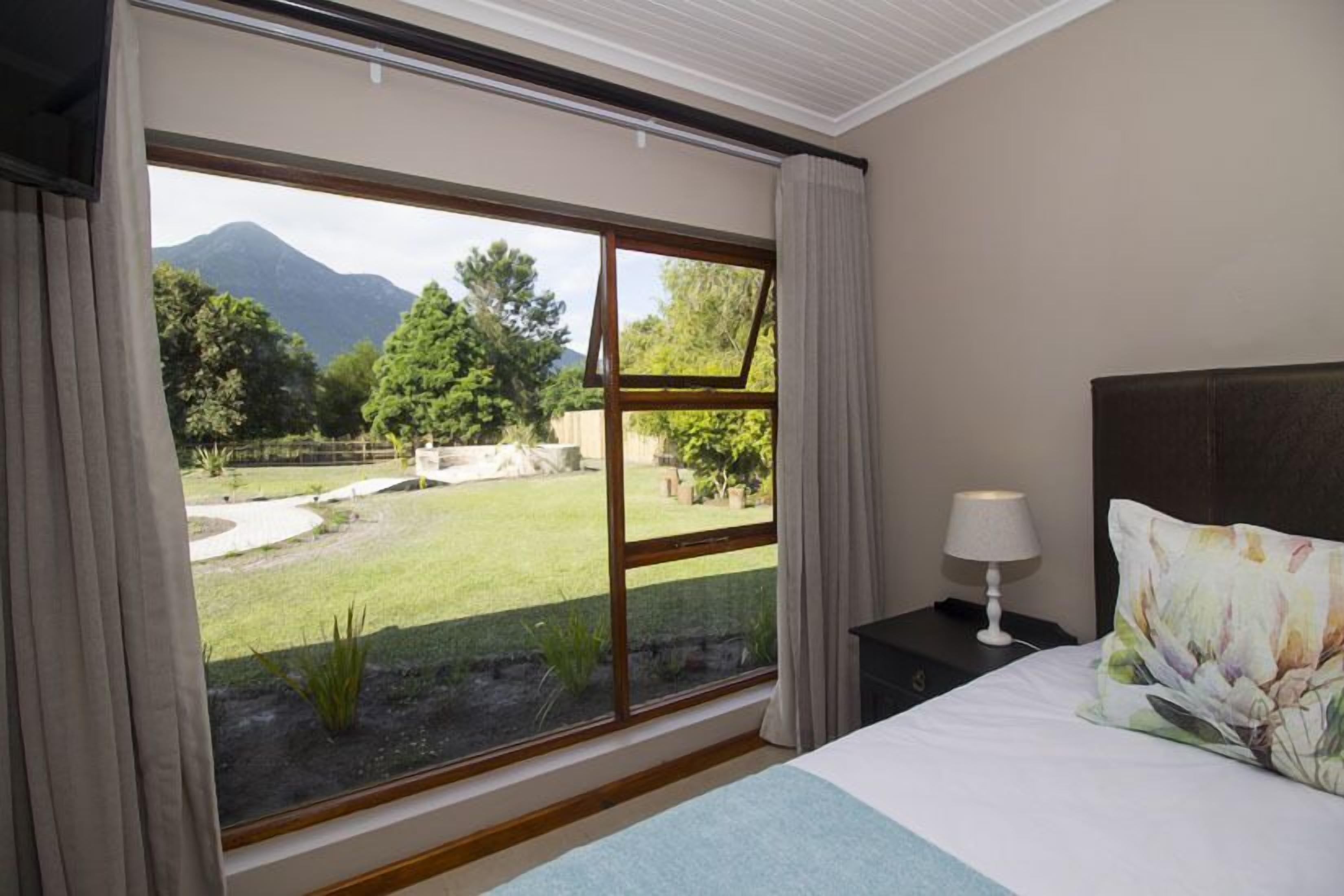 A bedroom with a large window, a bed with a pillow, a nightstand, and a lamp.