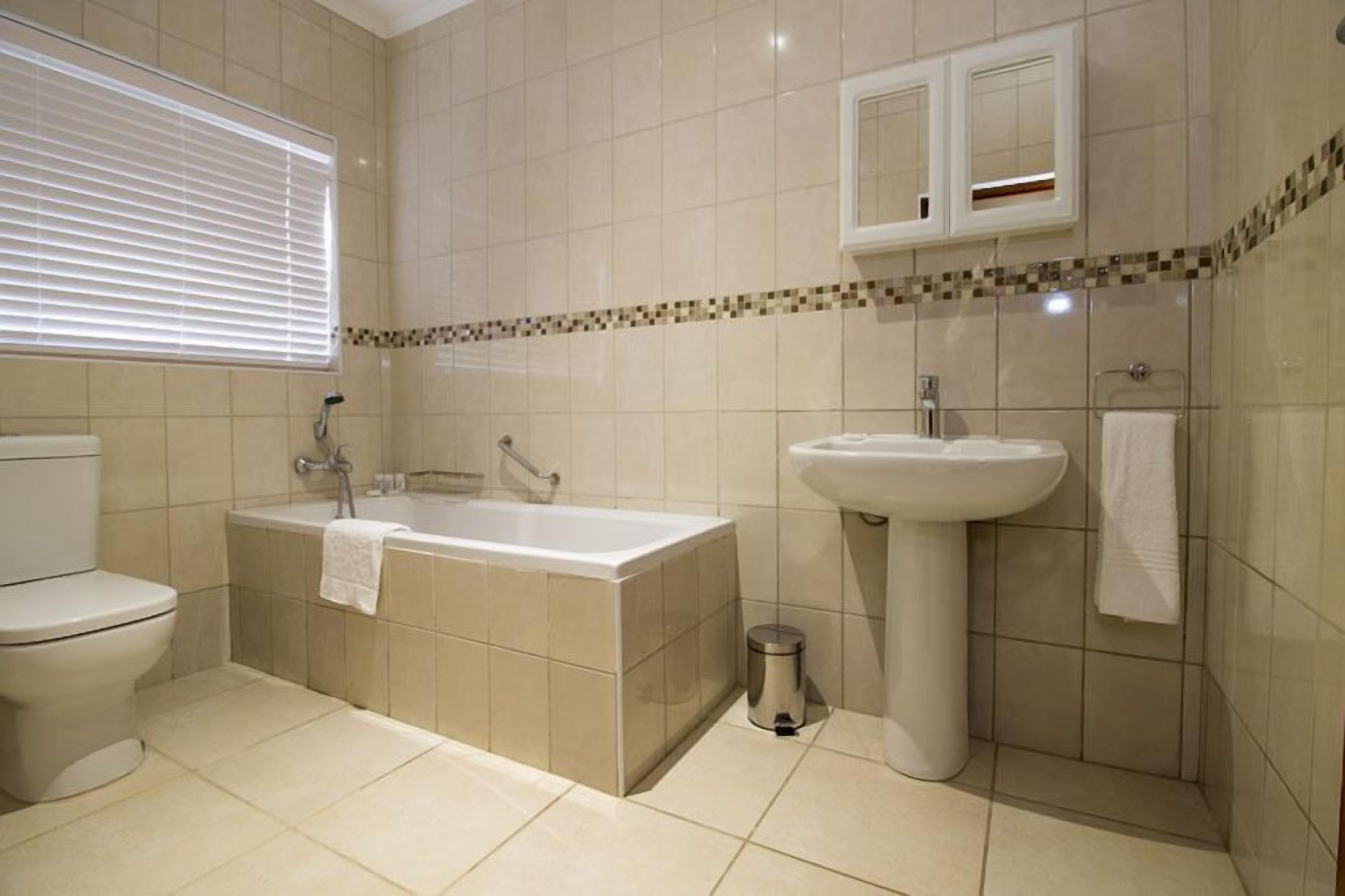 A bathroom with a toilet, bathtub, sink, and a window with blinds.