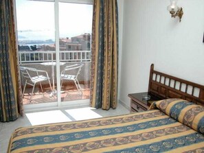 A bedroom with a bed, a nightstand, a chair, and a view of the outside through a glass door. - Ton (Sanxenxo)