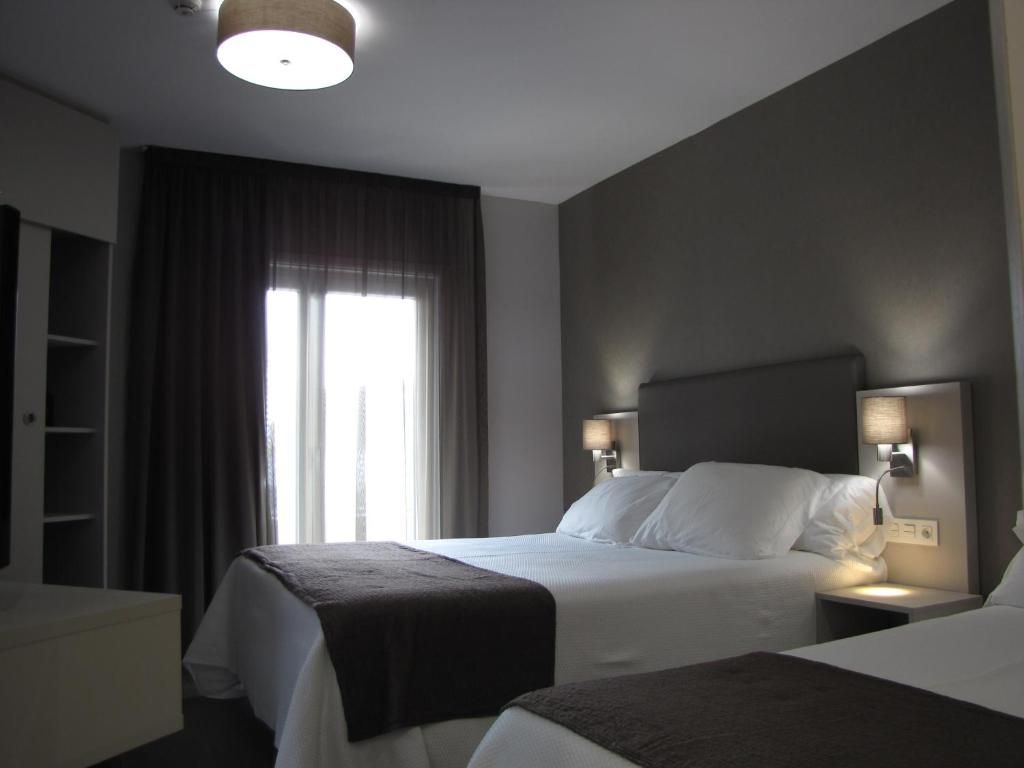 Habitación de hotel con una cama grande, lámparas de noche, un armario y una ventana con cortinas.
