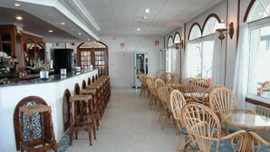 A spacious restaurant with a long counter and multiple tables with wicker chairs. - Ton (Sanxenxo)
