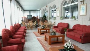 A hotel lobby with red sofas, wooden tables, and wicker chairs. - Ton (Sanxenxo)