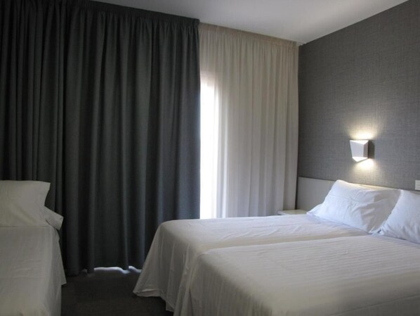 Ein Hotelzimmer mit zwei Betten, einem großen Fenster mit Vorhängen und einer Wandleuchte.