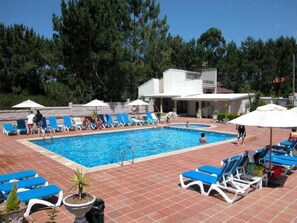 Ein Swimmingpool mit blauen Liegestühlen und Sonnenschirmen, umgeben von Bäumen und einem Gebäude.