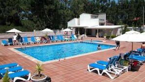 A swimming pool with blue lounge chairs and umbrellas, surrounded by trees and a building. - Ton (Sanxenxo)