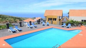 A pool area with lounge chairs and a view of the ocean.