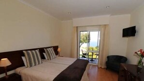 A hotel room with a large bed, a flat-screen TV mounted on the wall, and a balcony with a view.