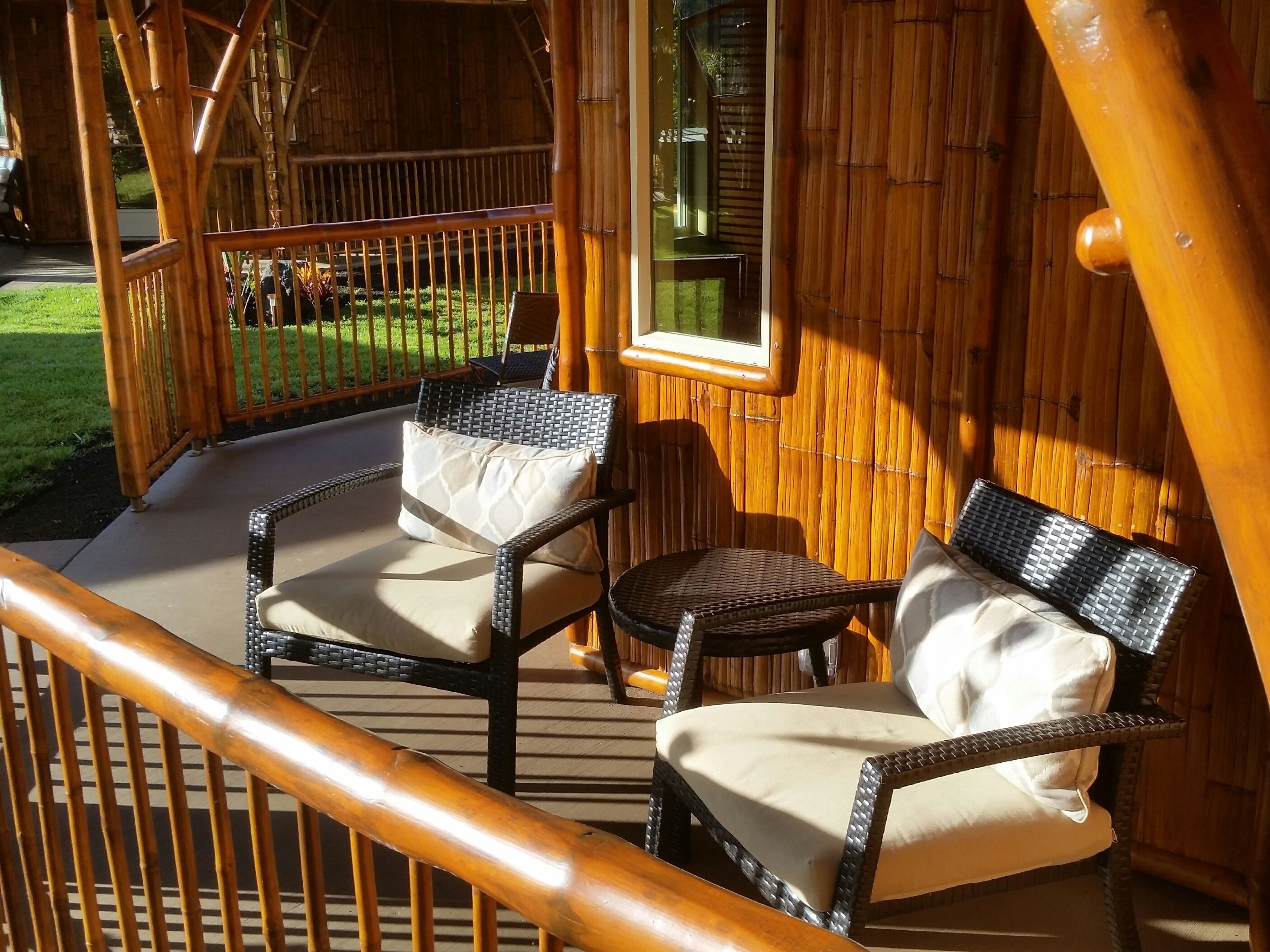A wooden deck with wicker chairs and a small table, surrounded by a bamboo fence.