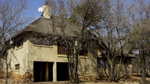 A house with a thatched roof, a garage, and a stone wall. - Thabaledi Game Lodge (Beestekraal)