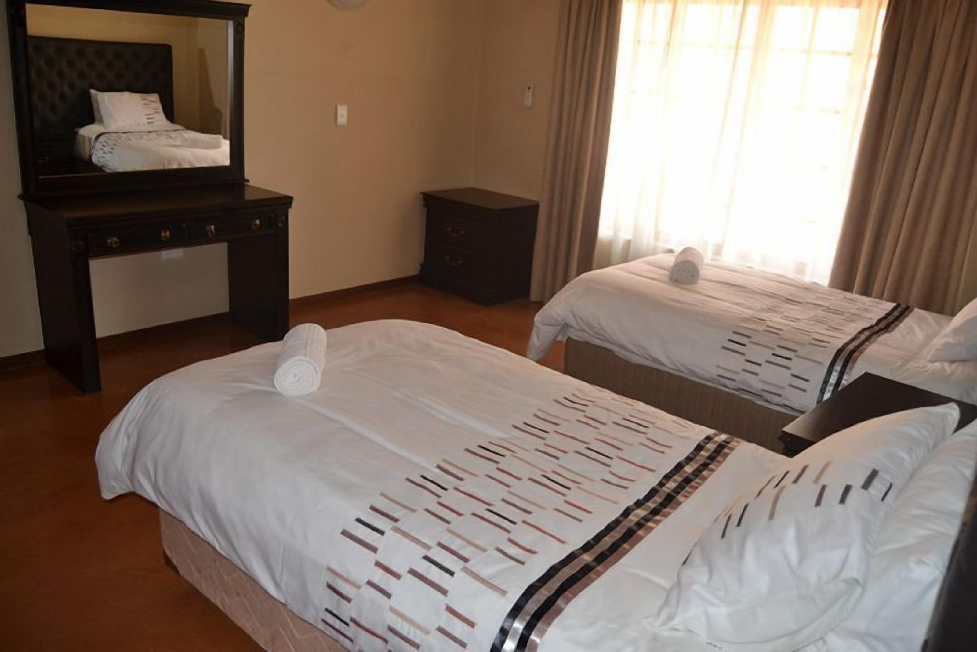 Habitación de hotel con dos camas, un escritorio con espejo, una mesita de noche y una ventana con cortinas.