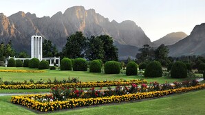 A landscaped garden with manicured lawns, flower beds, and a prominent building with a tower. - Fleur du Soleil (Franschhoek)