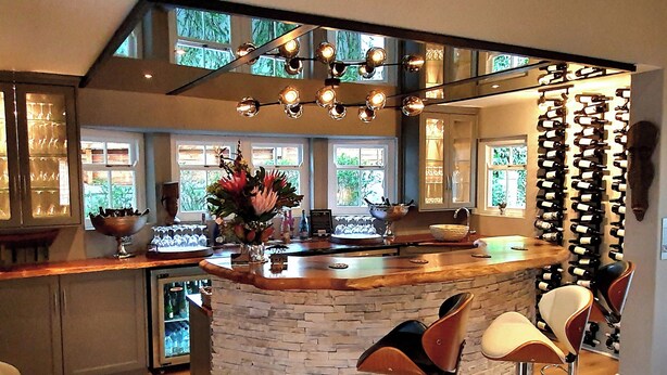 A modern kitchen with a bar area, featuring a stone island, bar stools, and a wine rack. - Fleur du Soleil (Franschhoek)