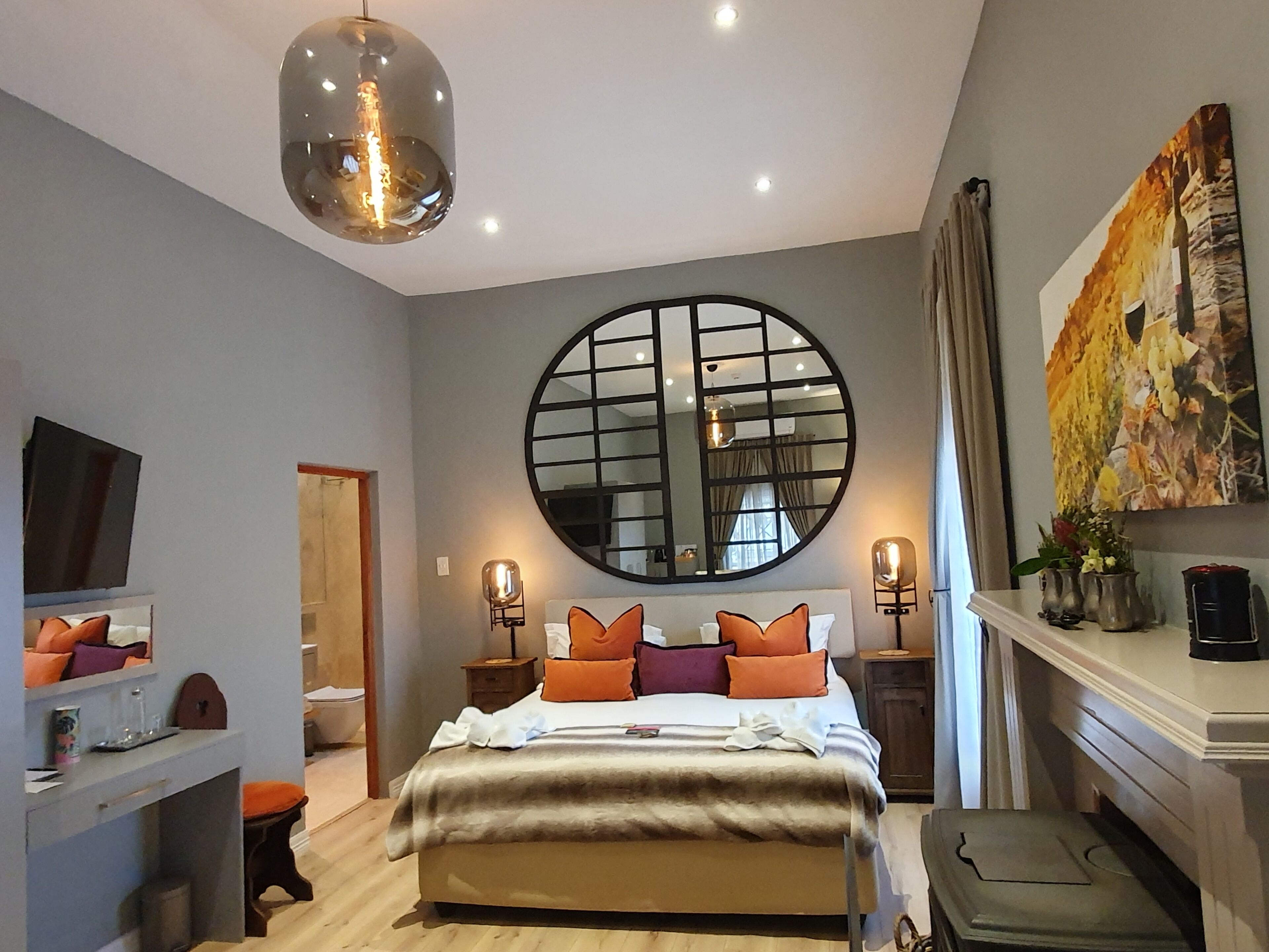 A modern bedroom with a large bed, a round mirror, a television, and a fireplace.