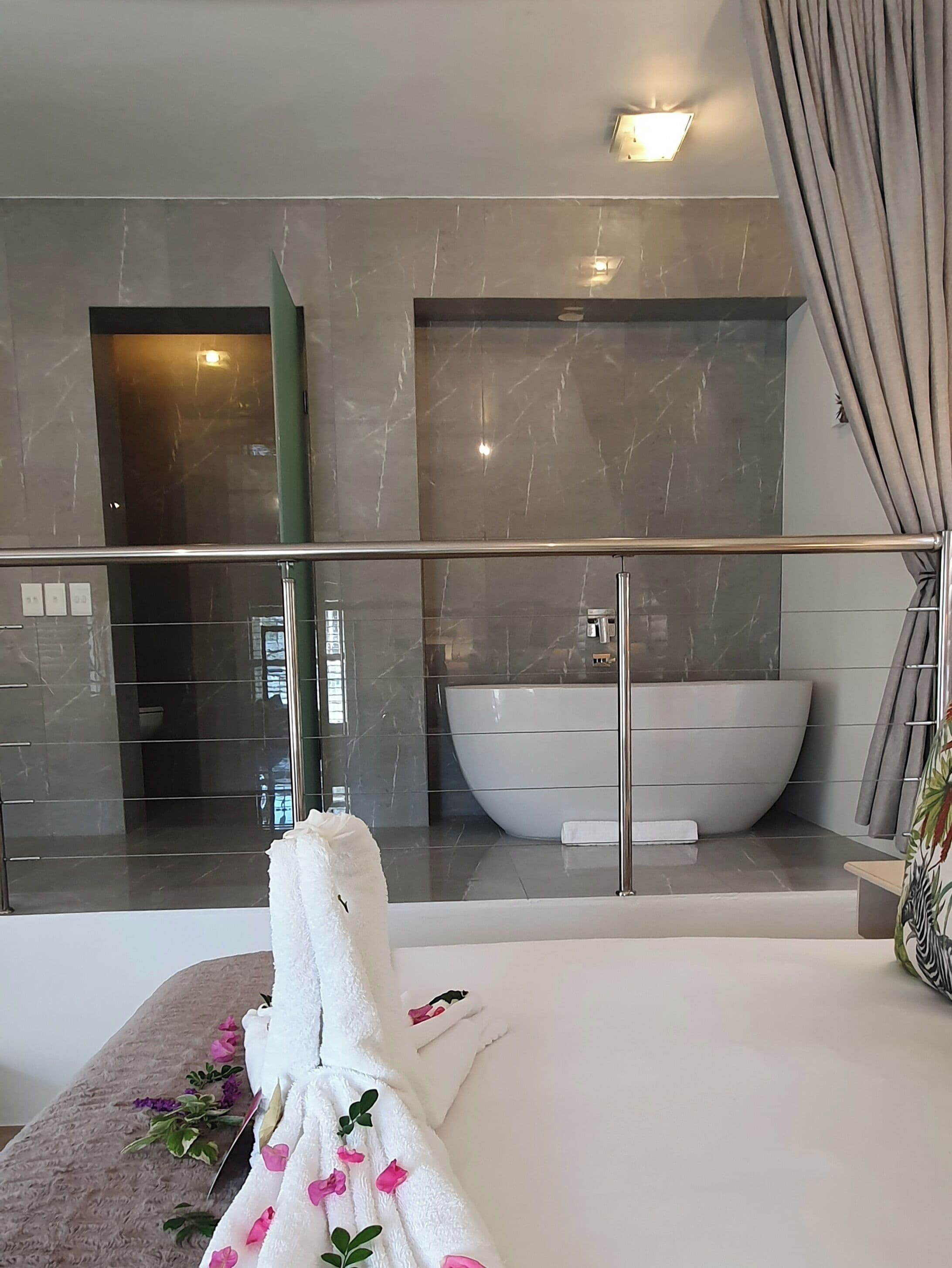 A modern bathroom with a large bathtub, a glass-enclosed shower area, and a balcony with a view.