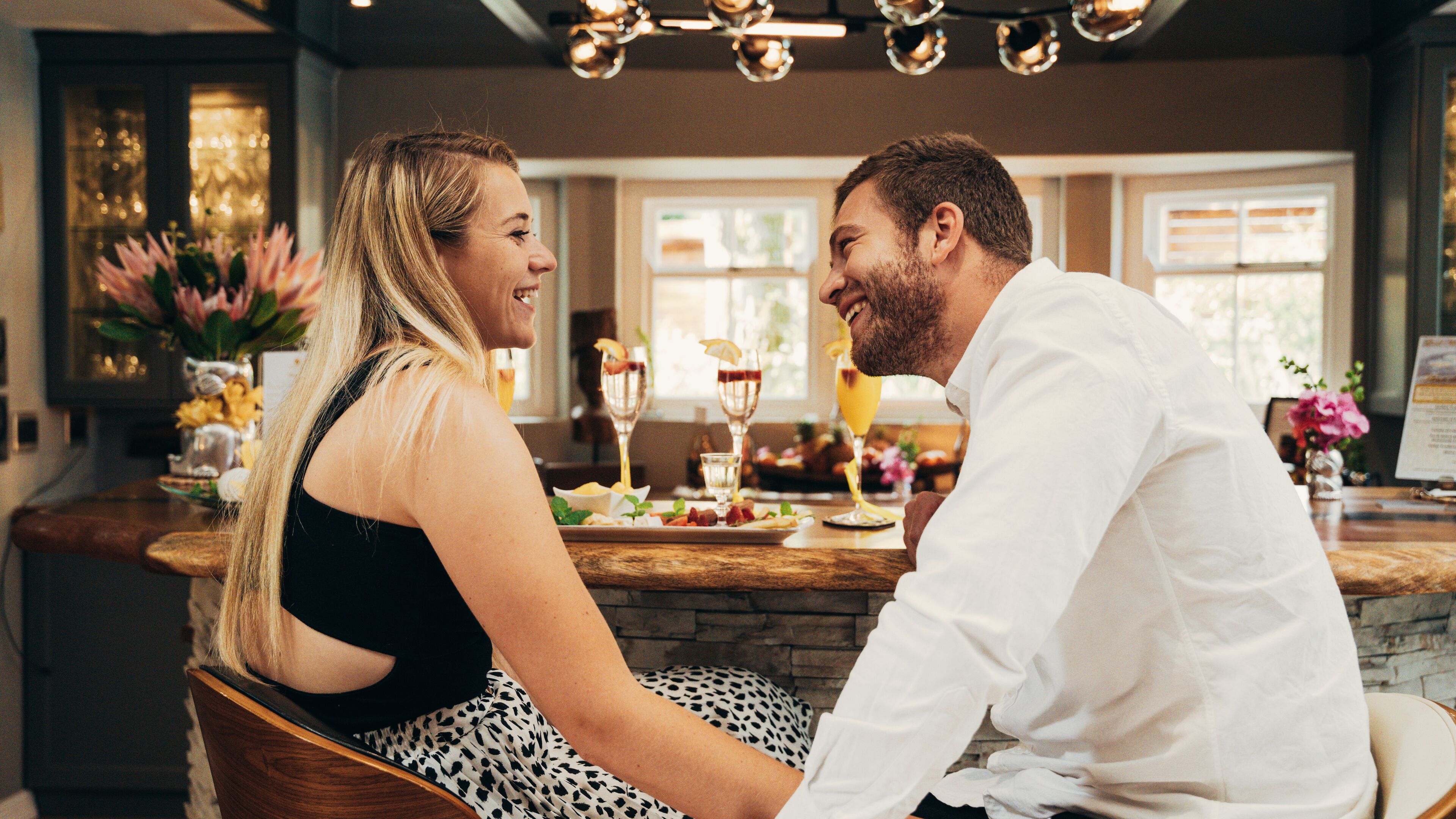Una pareja sentada en la barra, con diversas bebidas y un menú al fondo.