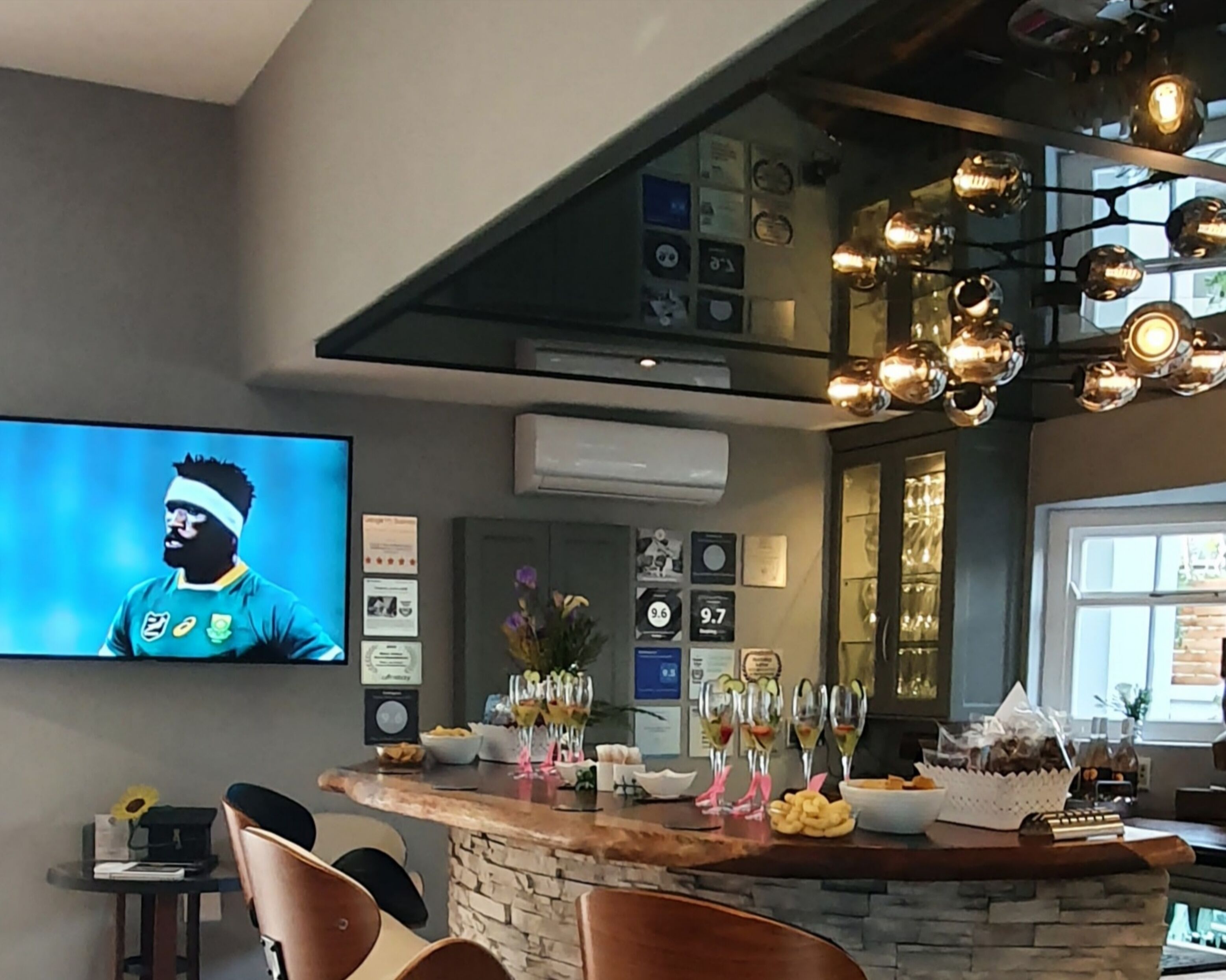 A modern bar area with a stone countertop, a television displaying a sports event, and various awards and certificates on the wall.