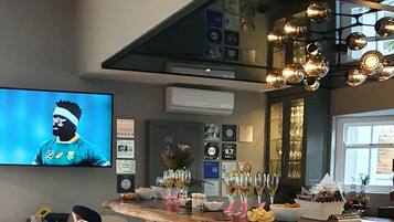 A modern bar area with a stone countertop, a television displaying a sports event, and various awards and certificates on the wall.
