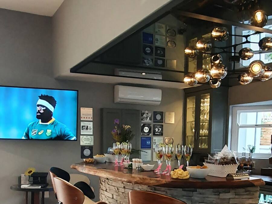 A modern bar area with a stone countertop, a television displaying a sports event, and various awards and certificates on the wall.